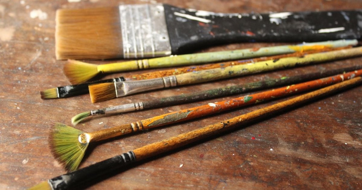 A row of used decorating brushes with dried paint on the bristles, laid out on a workbench