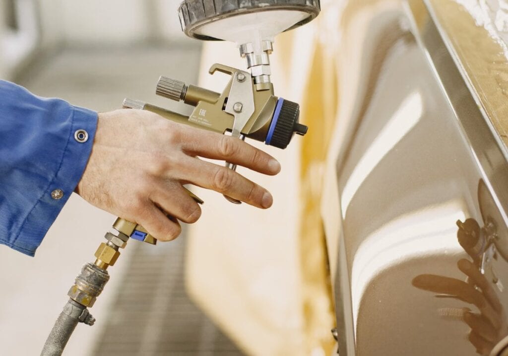 Gravity-feed HVLP spray gun laying down an even coat, the setup where cap pressure and inlet pressure get confused.