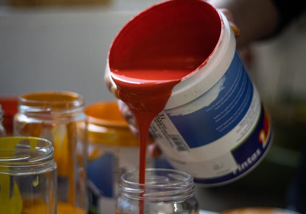 Red paint being poured from the can into a glass measuring jar before the thinner goes in, ready for a ratio by volume.