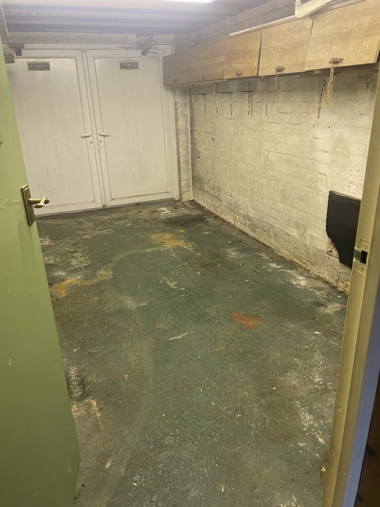 Garage with a damp stained concrete floor, bare block walls and an exposed timber beam, before treatment and painting