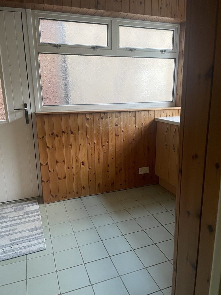 Utility room clad floor to ceiling in pine tongue and groove boards, with a window above the worktop, before painting